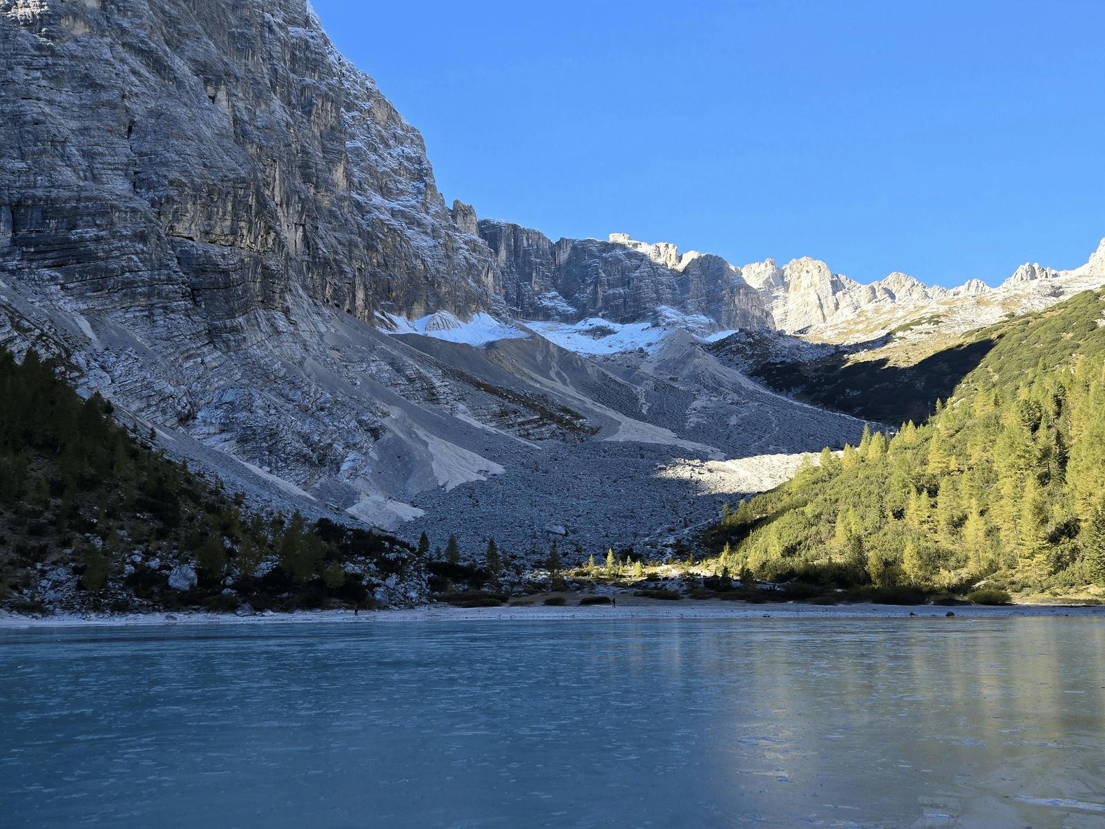 Snow-capped mountain reflected in a calm alpine lake under a clear blue sky.