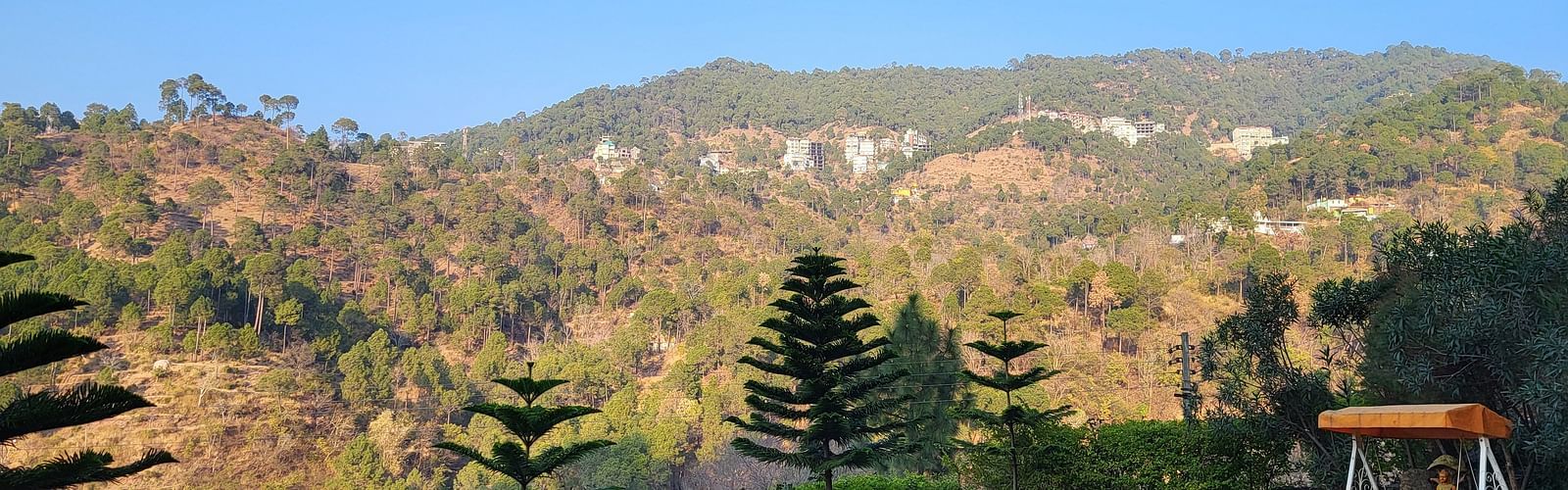 A scenic outdoor garden with a swing, white chairs, and mountain views at Dagshai Manor Kasauli - Inde Hotels.