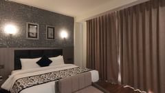 A room at Grand Continent, Anjuna featuring a large bed, a small sofa, dark curtains, and patterned walls with decorative lights.