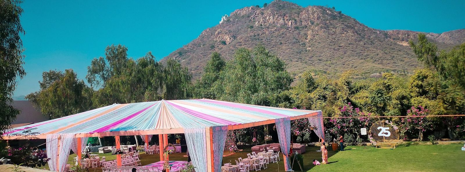 A tent with pink accents on a green lawn with a mountain view.