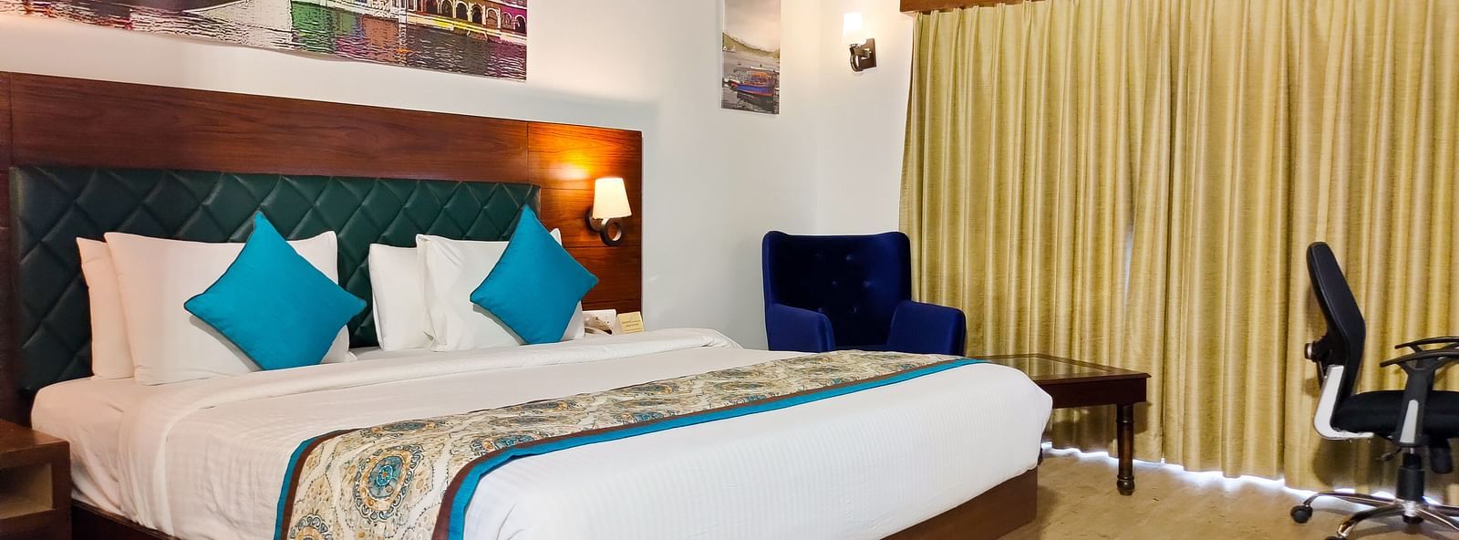 A hotel room featuring a large bed with pillows, a desk, and a armchair. - Bamboo Saa Resort & Spa, Udaipur