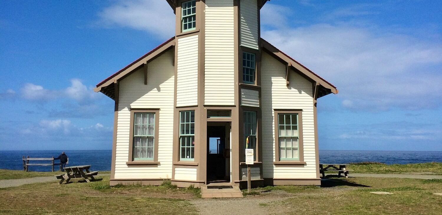 The front view of a high-ceilinged building with a grassy front yard on a sunny day.