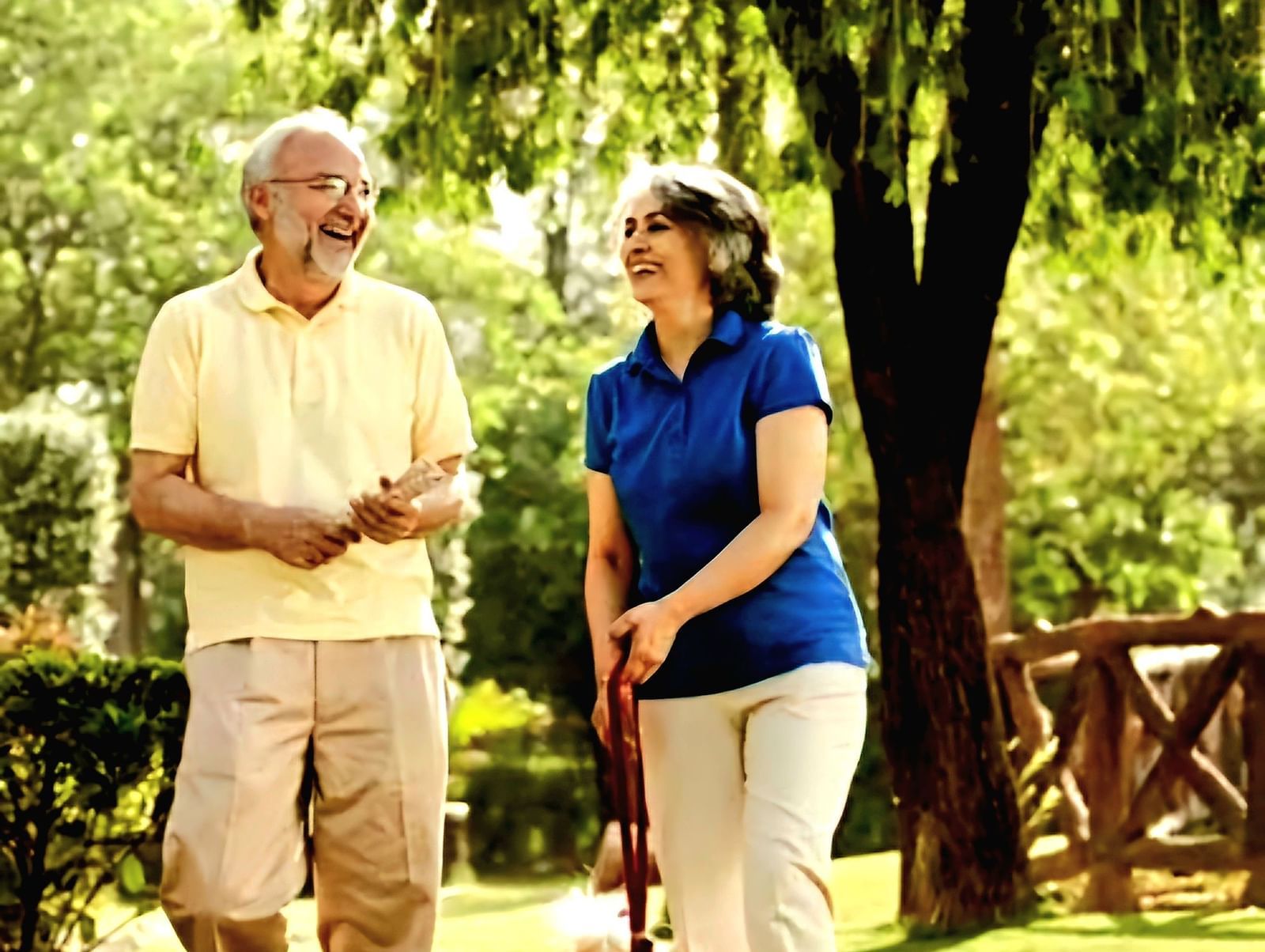 An old couple wearing western attire, walking a dog in a lush green park | Vedic Village Spa Resort