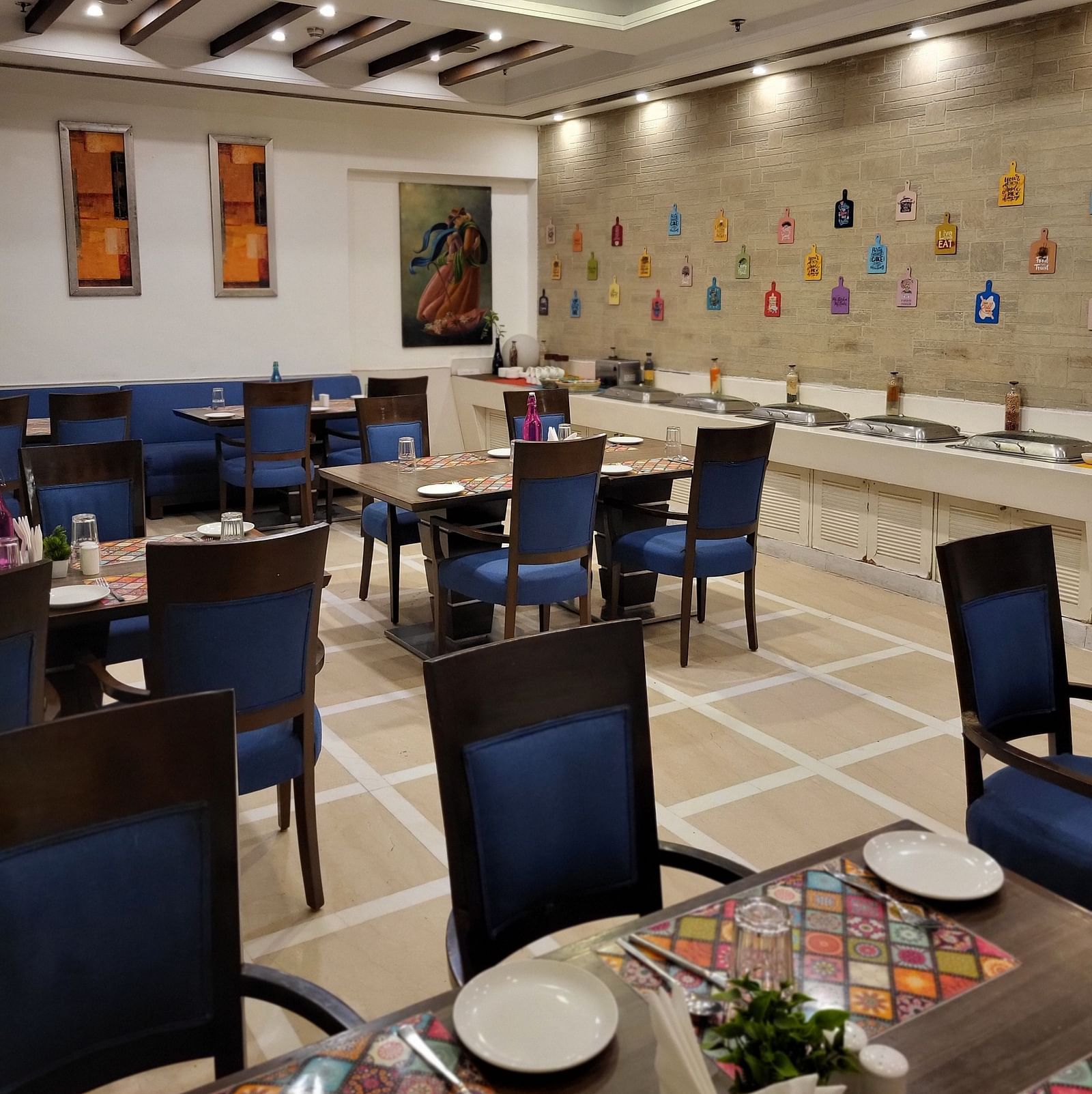 An image of a restaurant featuring multiple sets of chairs and tables where plates, cutlery and napkins are placed at Inde Hotel Signature Tower Gurgaon