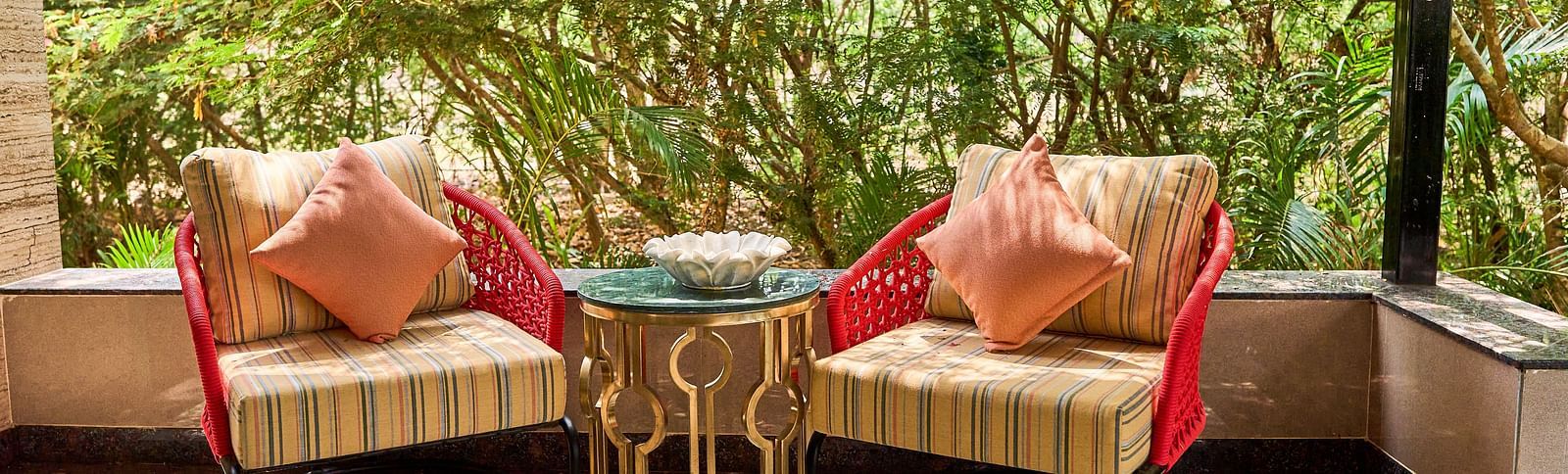 Two chairs placed beside the mini table, with lush trees as a backdrop at Mayfair Manor, Alibag