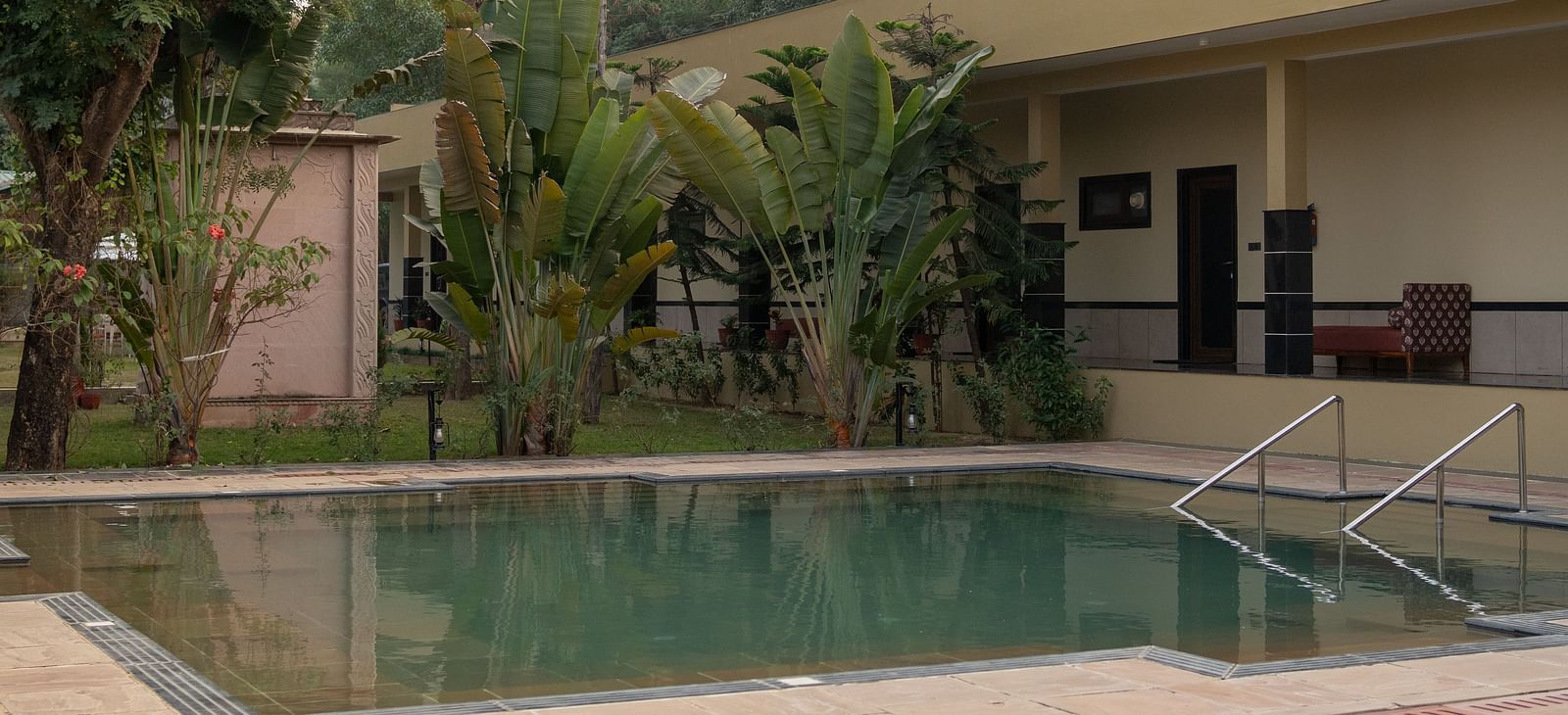 A serene swimming pool with steps leading into it at Aamaghati Jungle Retreat Ranthambore surrounded by greenery.