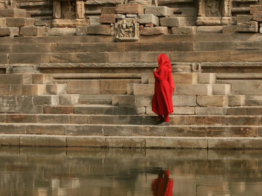 Chand Baori in Rajasthan  featuring woman in a red dress near the waterbody of a step well.