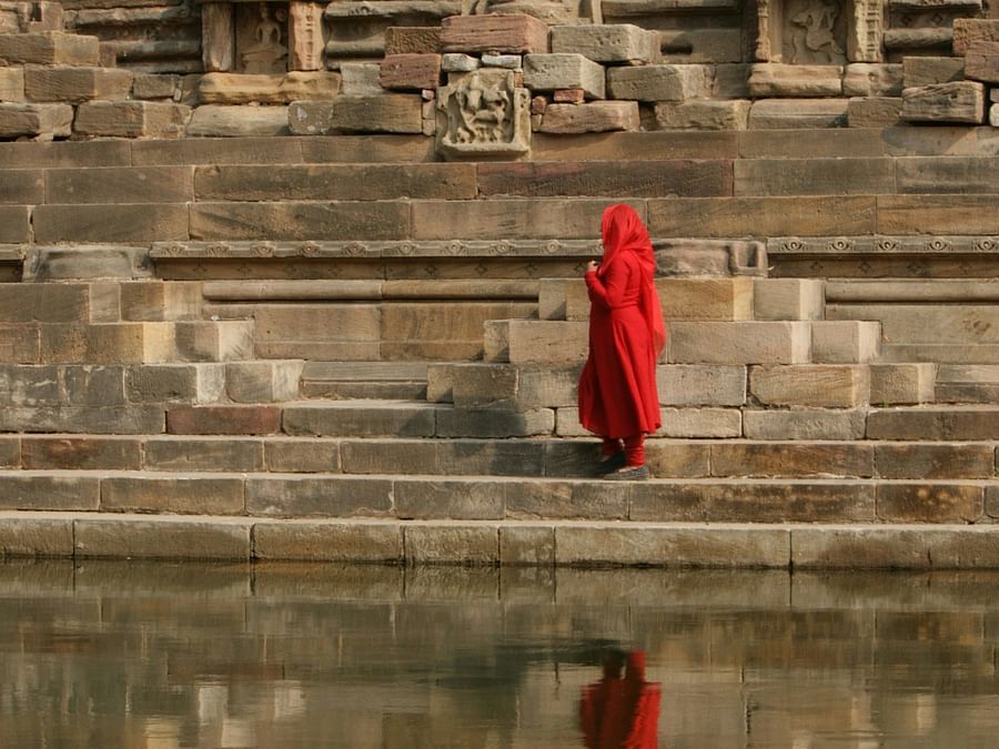 alt-text A woman in a red dress near the waterbody of a step well.