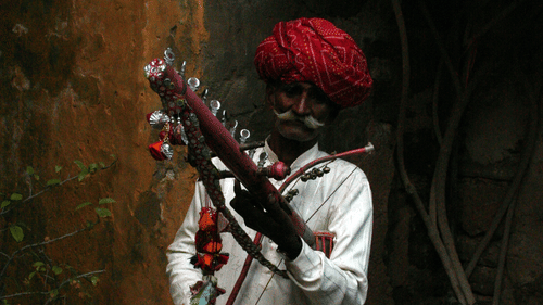 a man dressed in traditional Rajasthani attire playing a folk instrument