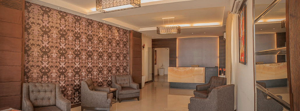 A waiting area with armchairs, patterned wallpaper, and a reception desk in the background | Astra Hotels and Suites Electronic City