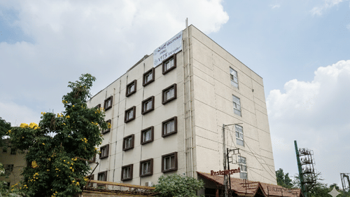 A hotel exterior view showing a multi-storey building with glass windows, tall trees and the VITS Select Bengaluru signage.