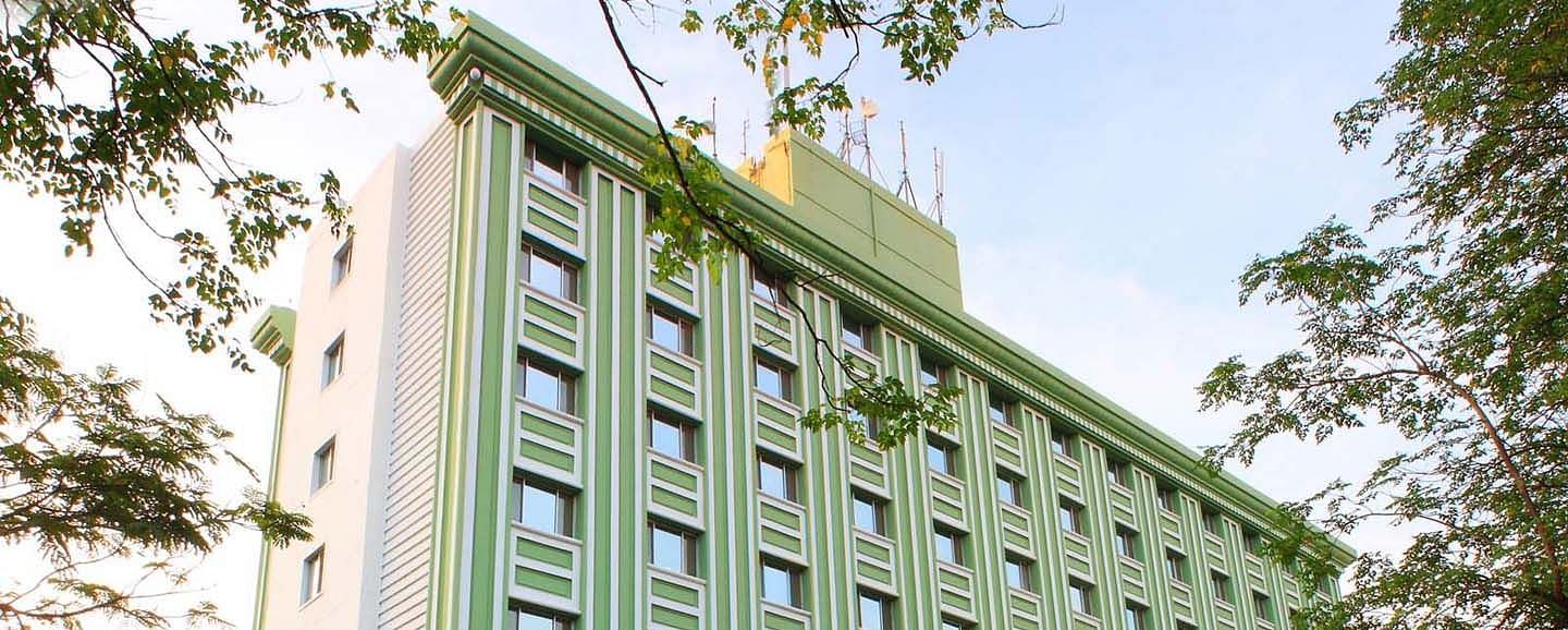 A multi-story green hotel building flanked by trees at Tara, Comfort Hotel in Hyderabad - Ramoji Film City.