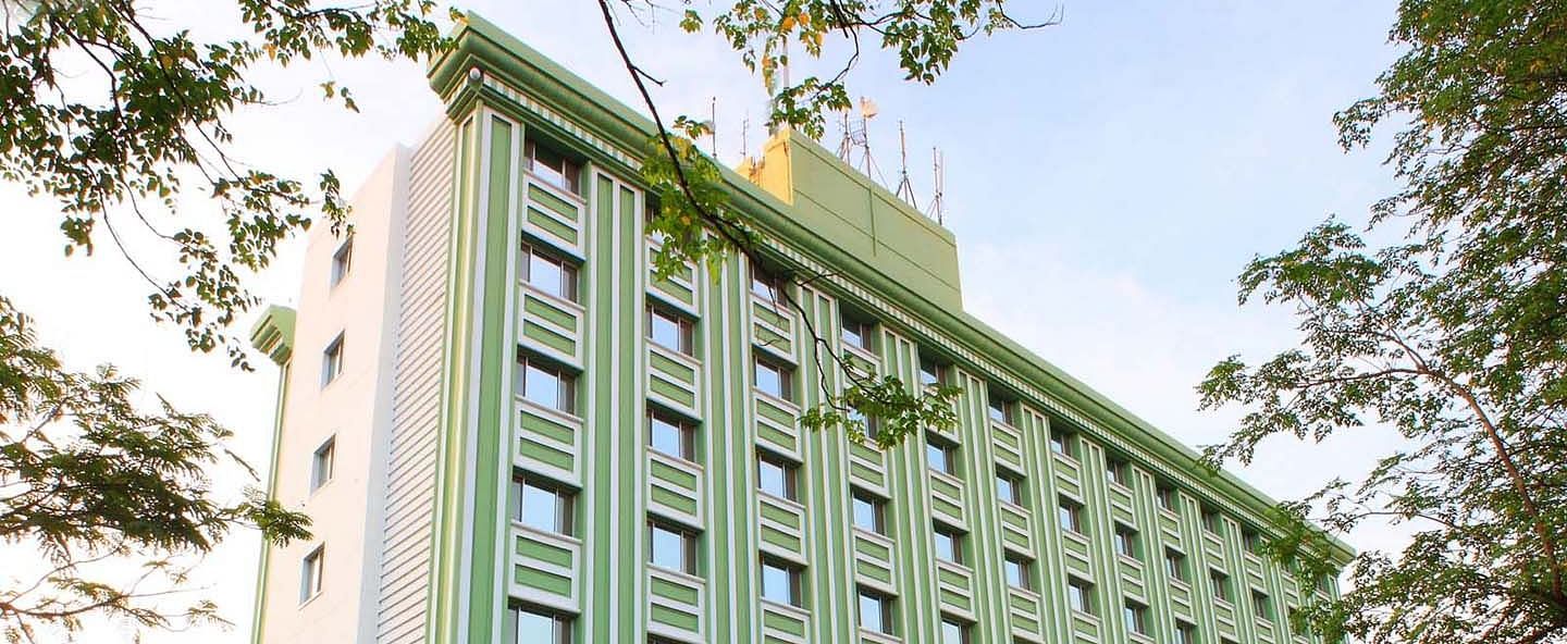 A multi-story green hotel building flanked by trees at Tara, Comfort Hotel in Hyderabad - Ramoji Film City.