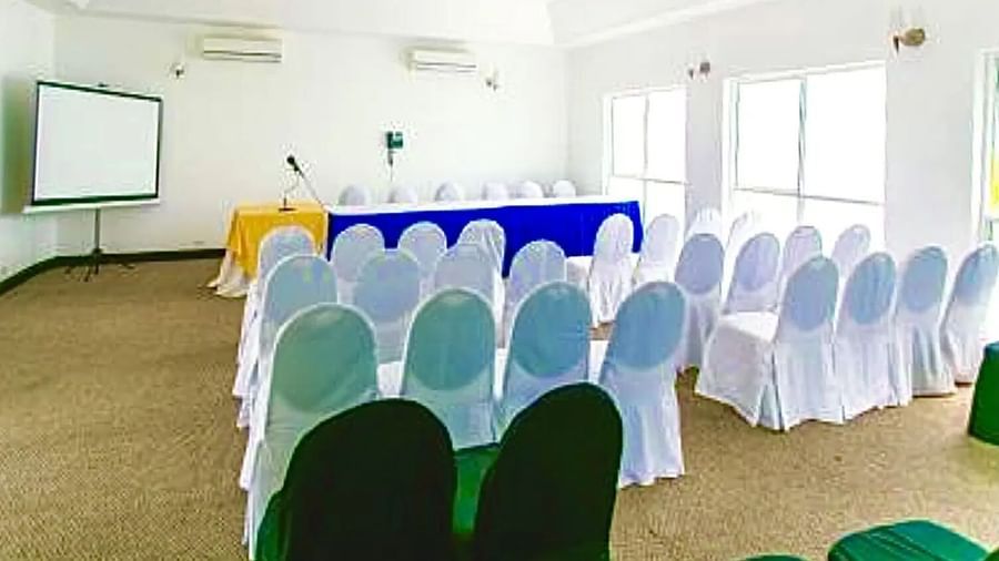A meeting room is set up with rows of white chairs facing a table with a white tablecloth and a projector screen | Karnak | Altamont Court, Jamaica