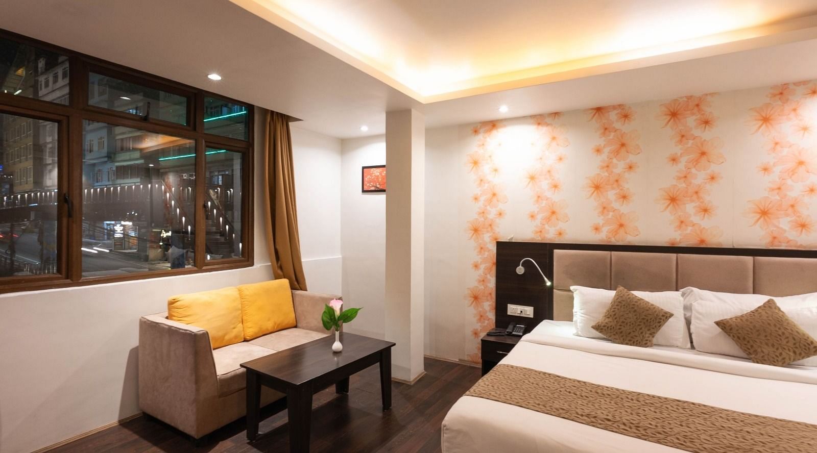 Deluxe Room at Avianna Hungry Jack, Gangtok featuring a plush bed next to a sitting space with a two-seater sofa and a coffee table by the window under warm lighting