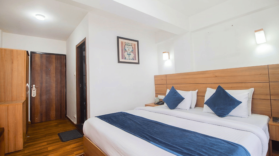 A room with double bed, Framed art work on the wall, TV, Wardrobe, Dustbin, Table and desk with two water bottles on the top at  Central Heritage Resort and Spa (Formerly Fortune ITC Resort) The Mall Ro