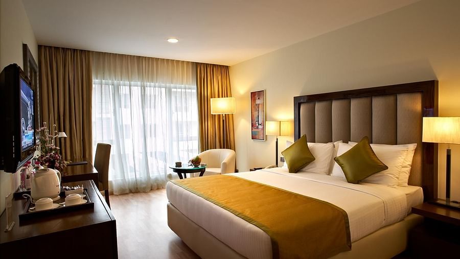 An image of a bedroom featuring double size bed, a flat TV screen, a cabinet, a sofa and centre table, and a few lamps at Adarsh Hamilton
