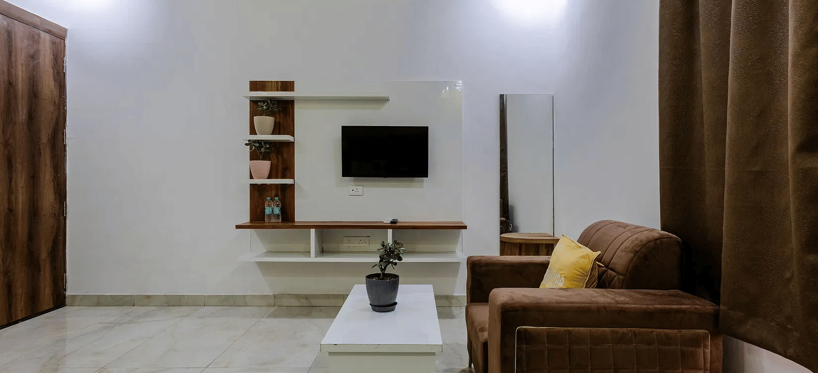 A living area with a sofa set, white centre table, and a television unit against the wall - Lime Tree Hotels & Banquet, Vrindavan