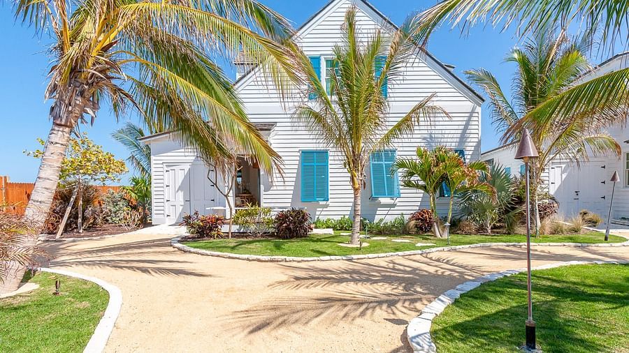 Exterior view of a white house with blue shutters, palm trees, and a sandy pathway | Abaco Inn