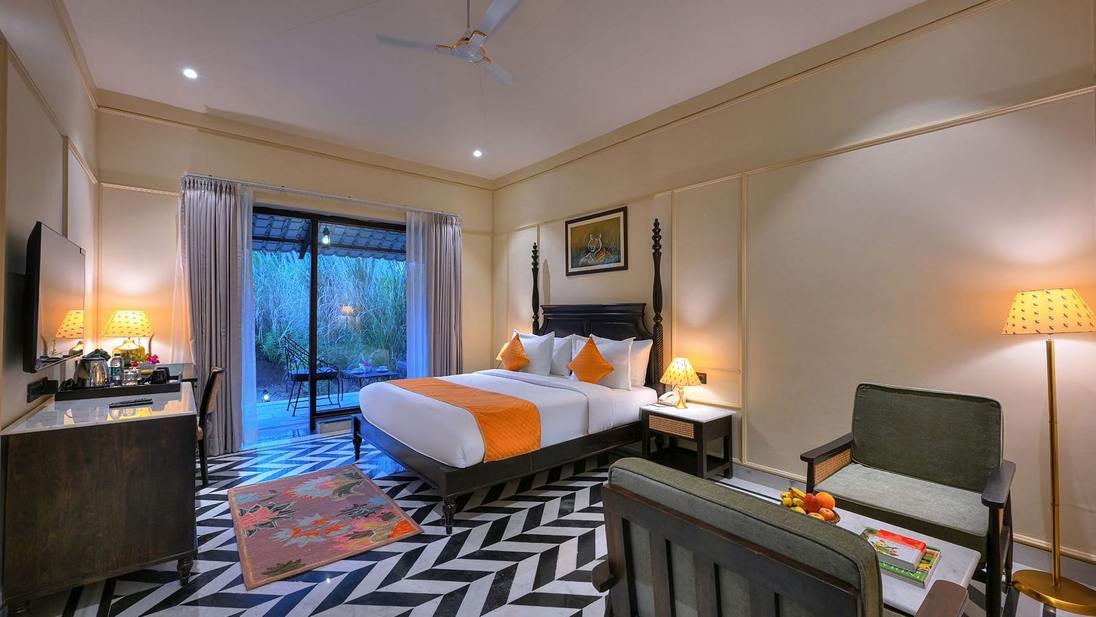 A well-lit Superior Cottage at Singhvilas with a four-poster bed, a black and white geometric floor, a work desk with amenities, and a balcony offering a view of the outdoors.