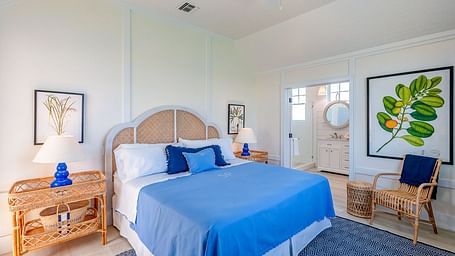 Bright bedroom with a woven headboard, blue bedding, wooden furniture, and framed botanical wall art | Abaco Inn