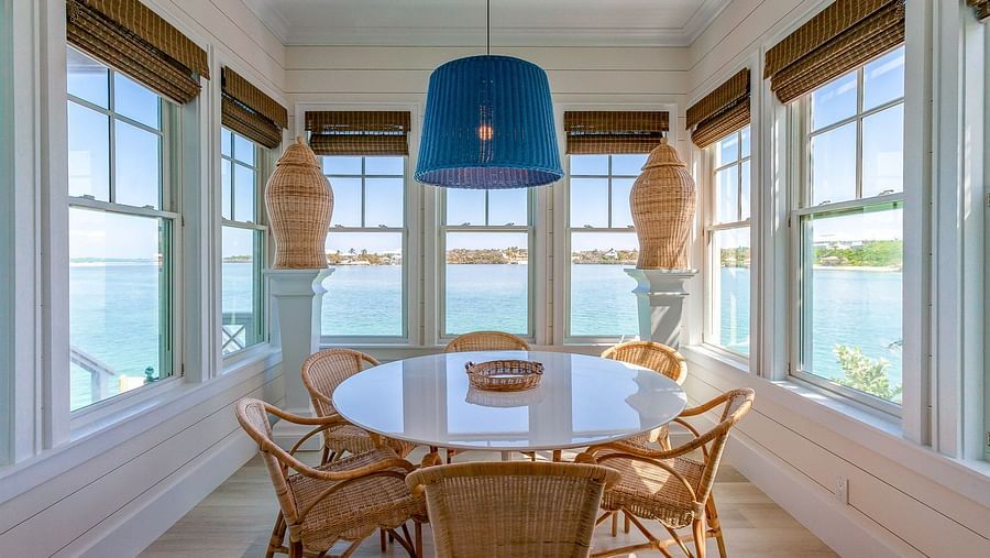 Dining area with a round table, wicker chairs, and ocean views through large windows | Abaco Inn