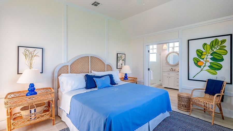Bright bedroom with a woven headboard, blue bedding, wooden furniture, and framed botanical wall art | Abaco Inn