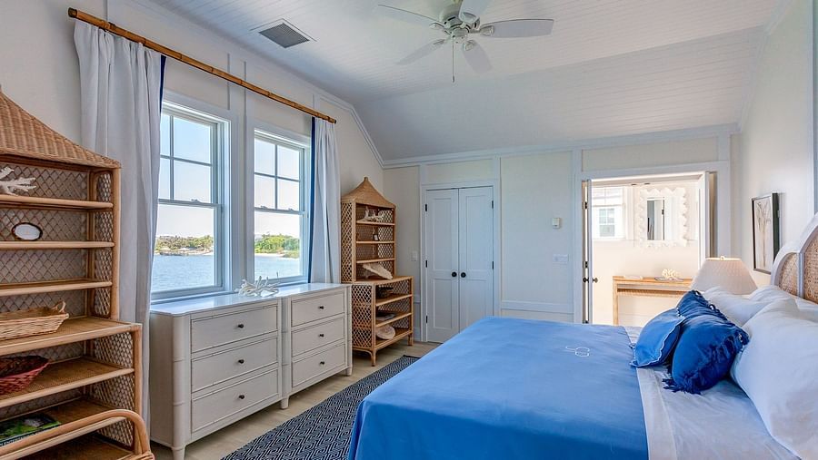 Bright bedroom with a blue bedspread, wooden shelving, and large windows allowing natural light | Abaco Inn