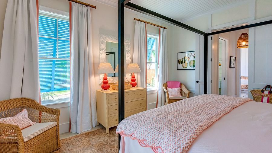 Bedroom with a pink-trimmed bed, wicker chair, red pendant lights, and large windows with curtains | Abaco Inn