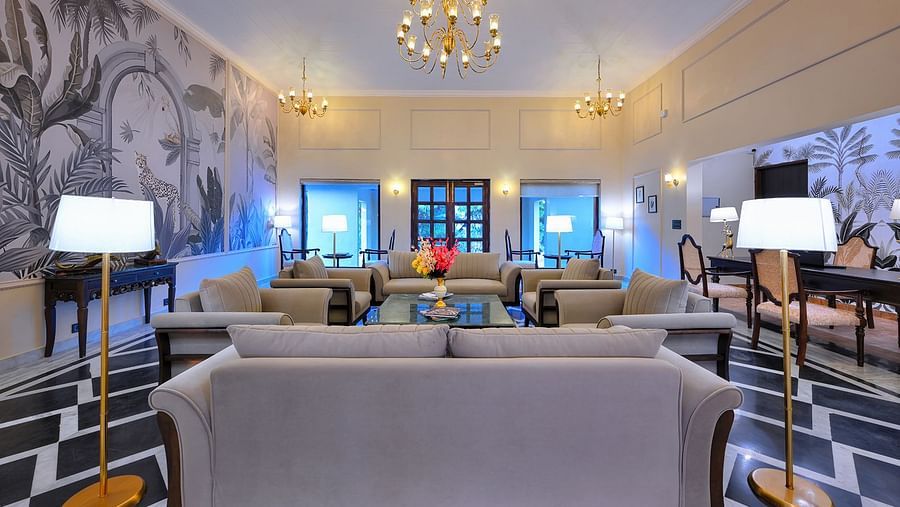 Elegant hotel lounge with beige sofas, chandeliers, floor lamps, and tropical-themed wall art at Singh Villas, Ranthambhore.