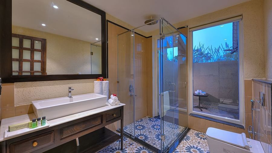 Luxurious bathroom of Superior Cottage at Singhvilas, Ranthambore, featuring a spacious vanity, glass-enclosed shower, elegant patterned flooring, and an outdoor sit-out area visible through large windows.