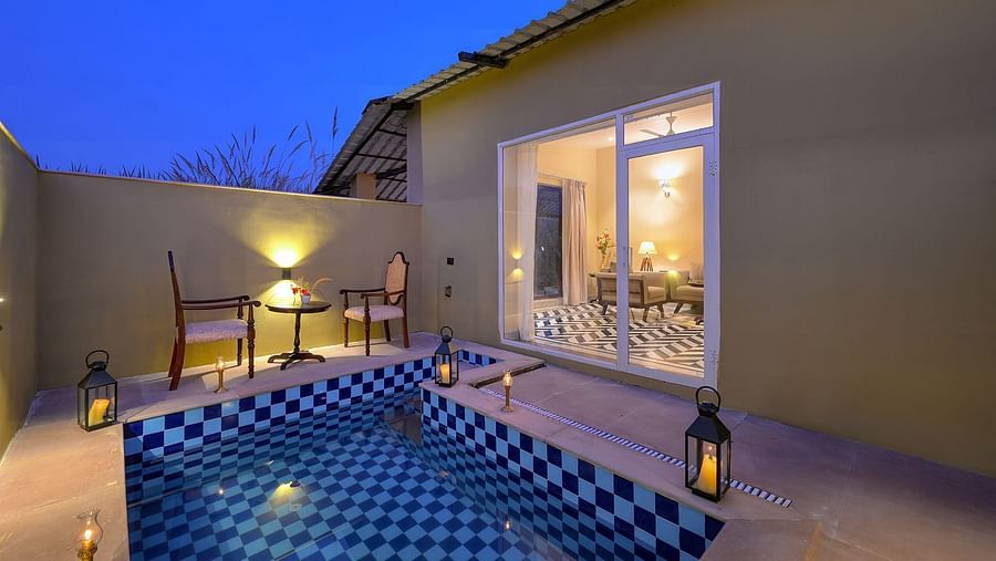A serene outdoor space of Premium Suite Cottage featuring a tiled plunge pool, cosy seating, and warm lanterns, illuminated by a twilight sky - Singhvilas, Ranthambore