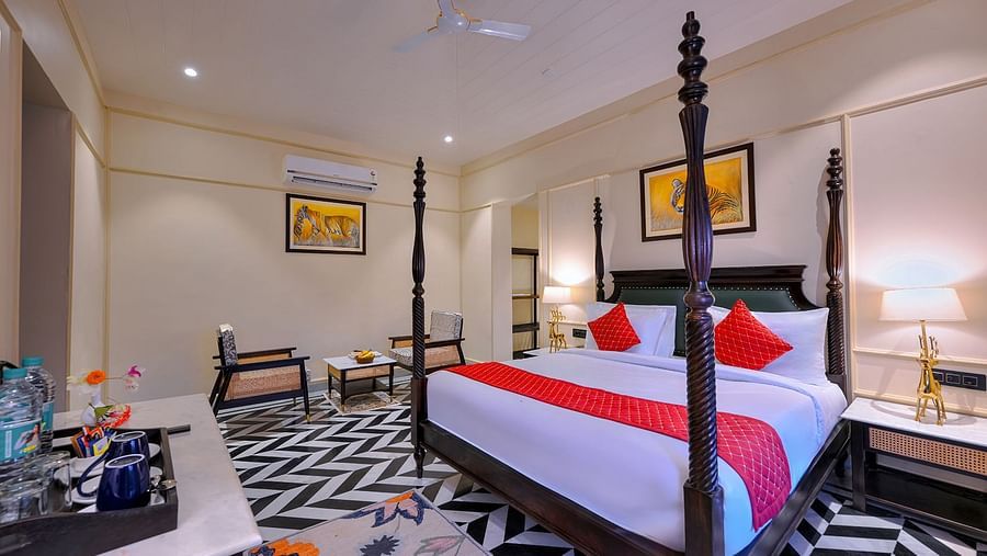 Premium Suite Cottage with a dark wood four-poster bed featuring red accents, black and white chevron flooring, a seating area with two chairs, air conditioning, and framed artwork - Singhvilas, Ranthambore