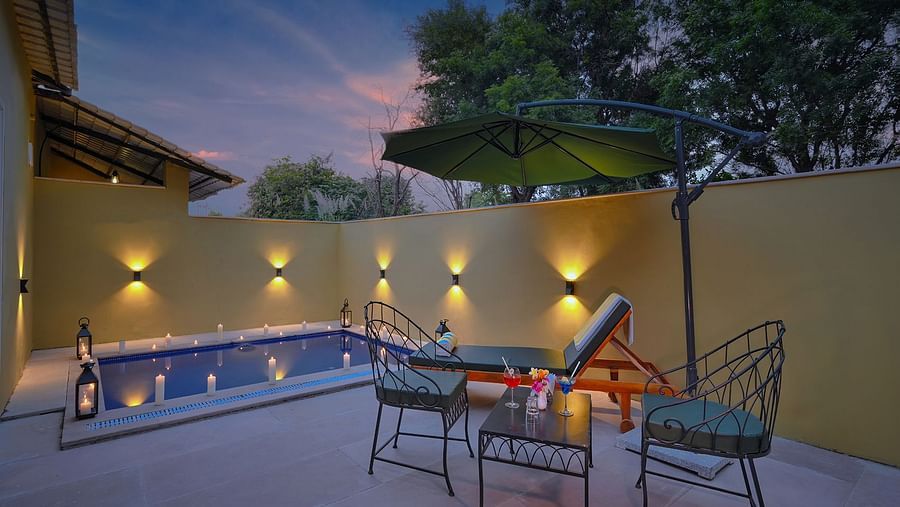 A secluded patio in Luxury Suite Cottage with a small, illuminated pool, lounge chairs, an umbrella, and outdoor lighting at dusk - Singhvilas, Ranthambore