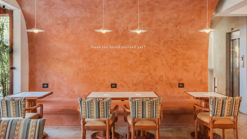 Book direct and get 31% off at Unseen Boutique Hotel Assagao Goa featuring a cozy seating area with two patterned armchairs a checkered rug and warm string lights on a wooden ceiling.