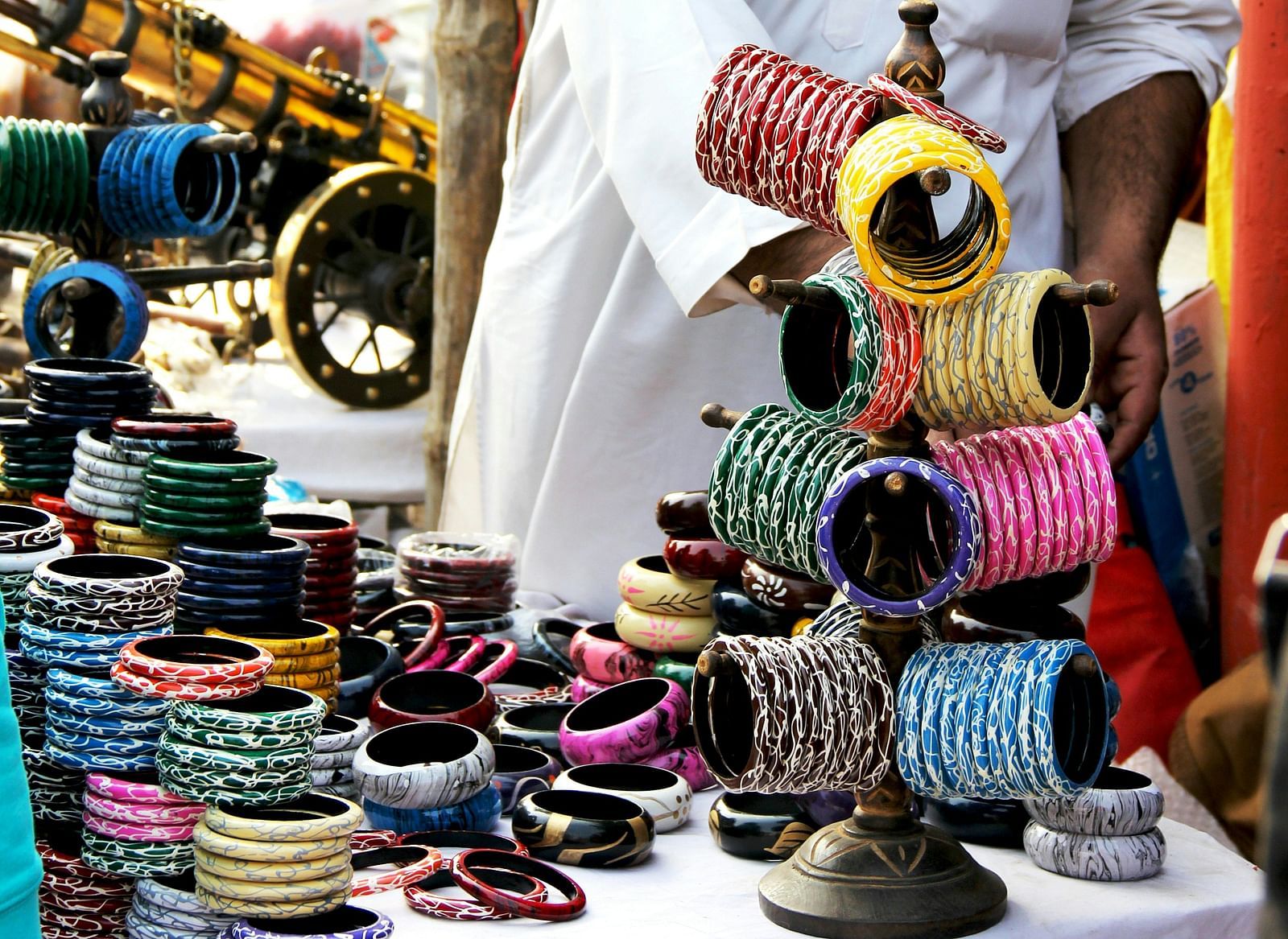 Close-up of numerous colorful bangles for sale, arranged on a white cloth-covered table.