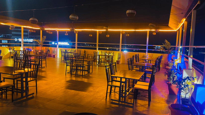 A dimly-lit dining area with empty tables and chairs, illuminated by blue and orange lighting - VITS Select Kailash Inn, Bagalkot