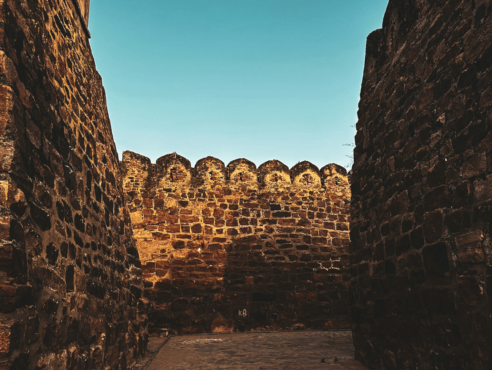 Interiors of a fortress with bricked walls and a pathway along with a clear blue sky in the background.