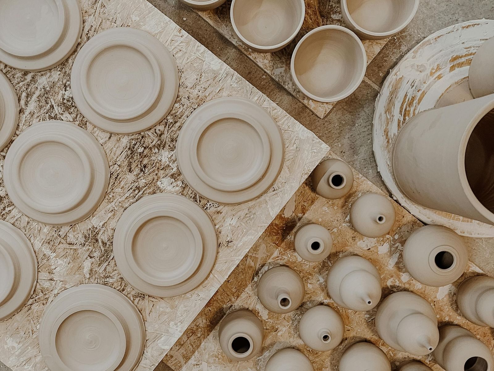 An overhead view of various unglazed ceramic or pottery pieces, possibly bowls and plates, arranged on a textured surface.