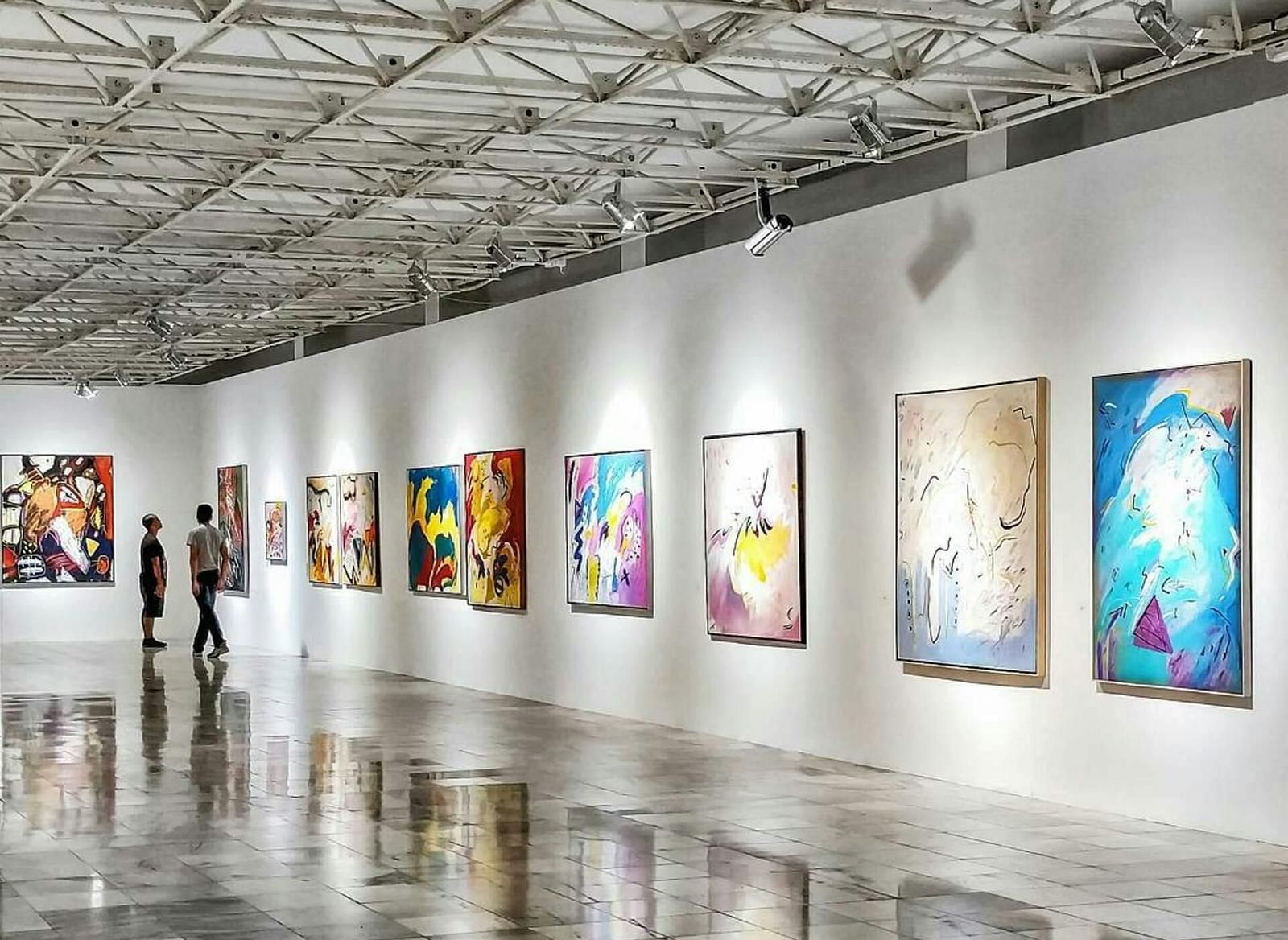 A brightly lit art gallery with white walls and several framed pieces displayed along the length of the room.