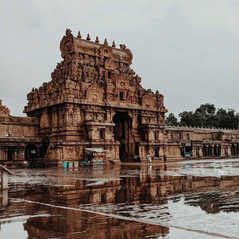 An ornate stone temple gateway reflected beautifully in a large puddle on the wet ground after rainfall