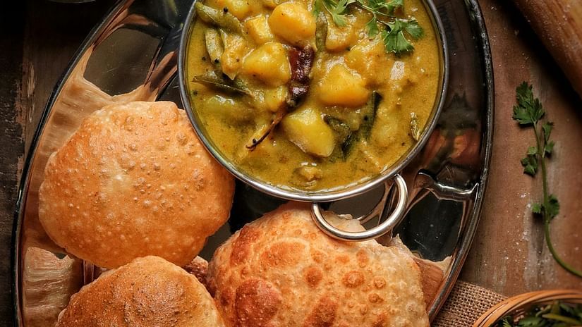 An image of three puris arranged on a plate served with a side of potato gravy.