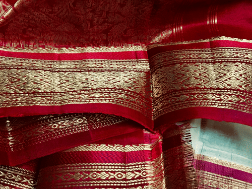 A silk saree with intricate gold zari brocade borders, traditional Indian textile shimmering under soft light