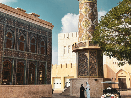 A tall, round, white minaret tower, set in an old-style town square with paved ground and buildings in Katara cultural village, a must-visit from the Doha 2 Day Itinerary.