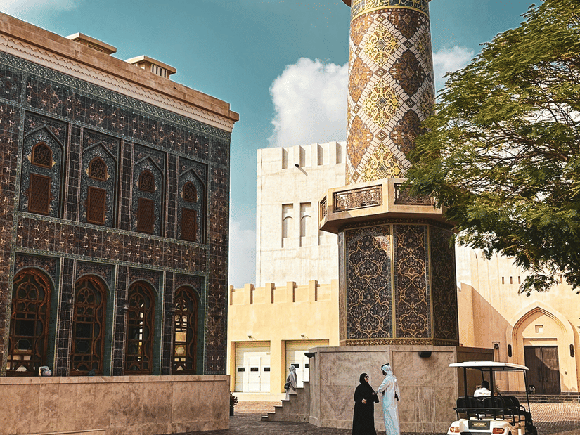 A tall, round, white minaret tower, set in an old-style town square with paved ground and buildings in Katara cultural village, a must-visit from the Doha 2 Day Itinerary.