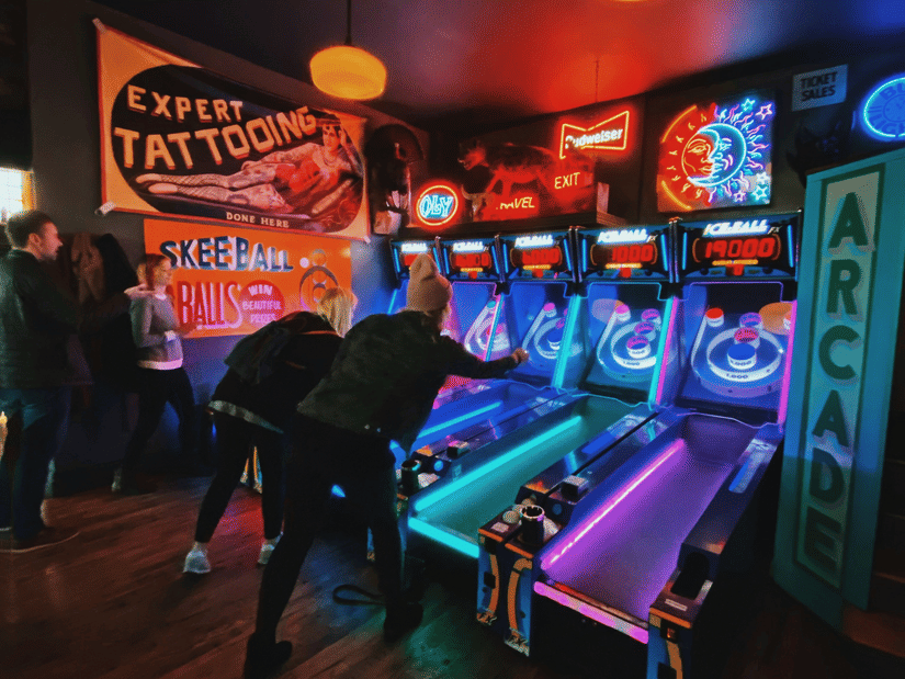 An overview of an arcade place with two guys playing games on the neon-lit machines.