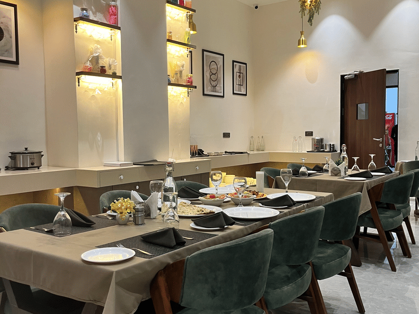 Seating arrangement at Aromas the best restaurant in Jamnagar at VITS, featuring cutlery and napkins placed on the dining table under warm lighting