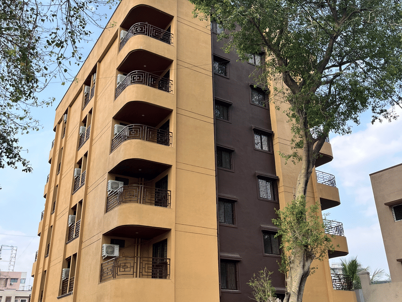 A multi-storey hotel building with curved balconies stands beside tall trees at VITS Select Kharadi, Pune.