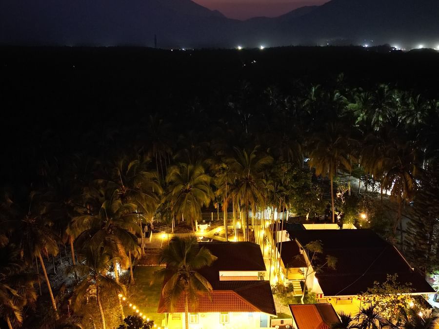 Aerial view of a resort at dusk with illuminated buildings and palm trees, set against a backdrop of mountains.