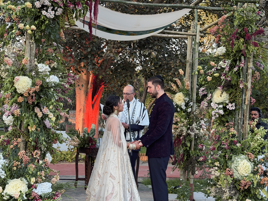 A bride and groom standing before a beautifully decorated outdoor floral altar with candles lining the aisle at Umaid Palace.